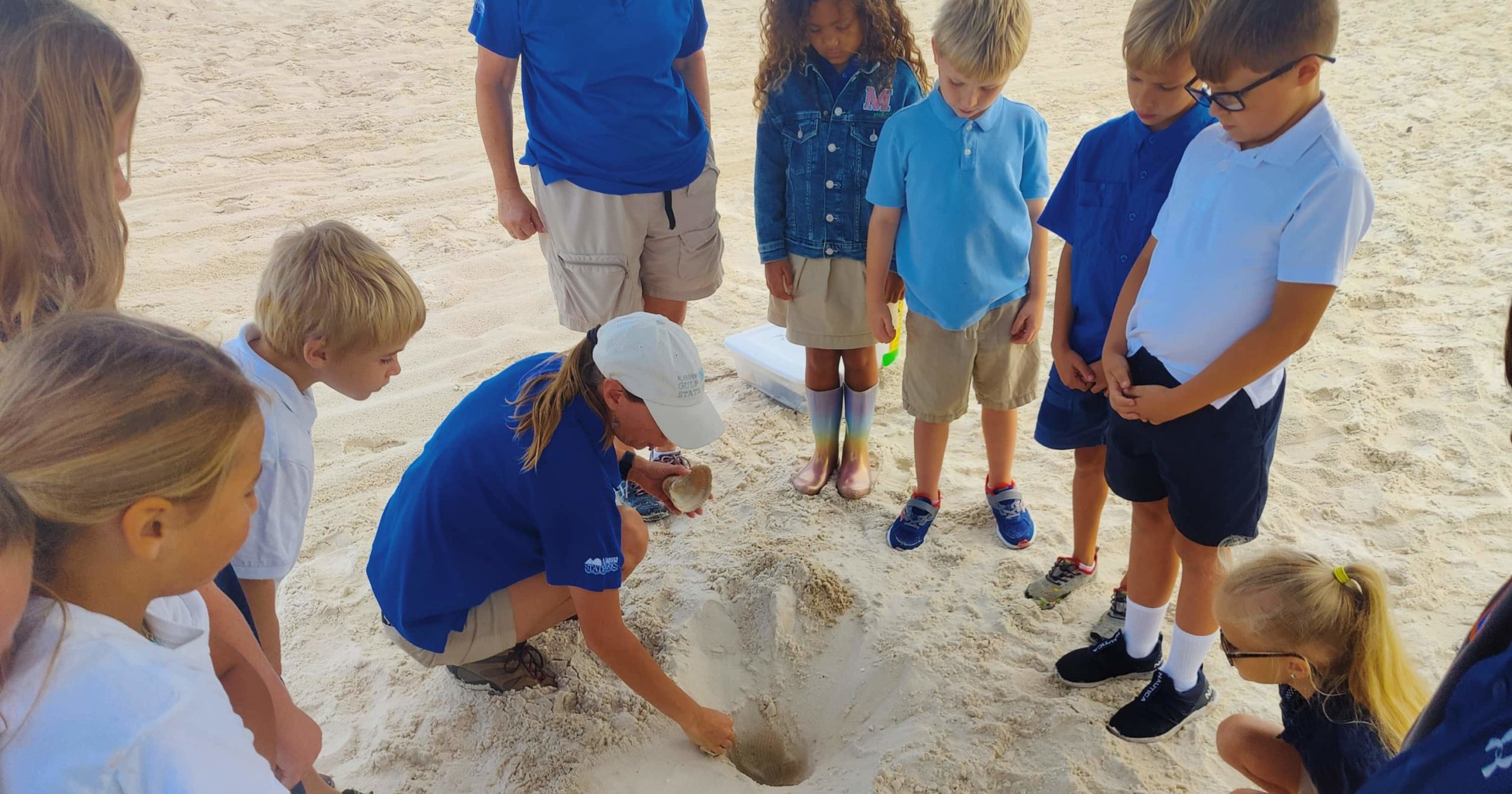 Kelly Reetz from the Gulf State Park demonstrates how sea turtles nest by digging a hole in the sand while a group of students observe her